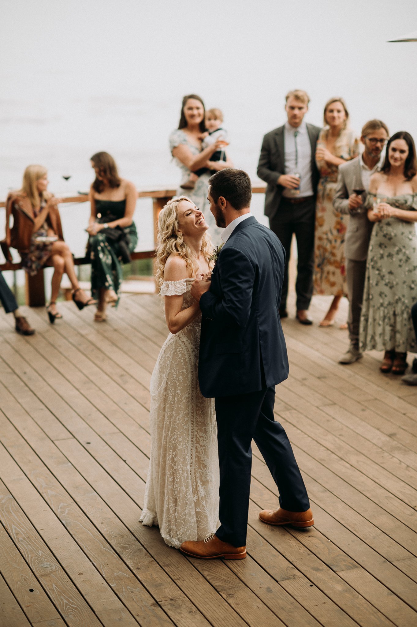 Bride and groom first dance on deck with guest watching and pacific ocean in background