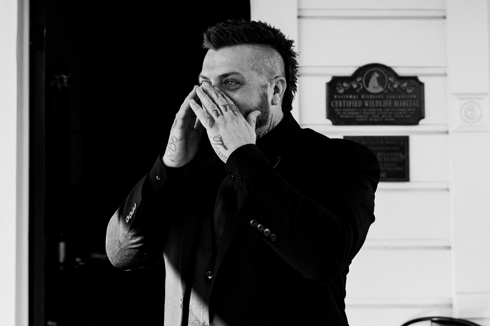 black and white photo of groom in wedding attire wiping tears from his eyes as he sees his bride at the first look on their wedding day.