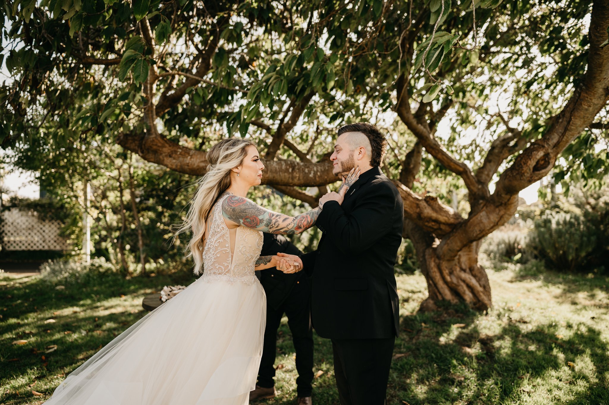 bride and groom at  outdoor altar in a garden under a shade tree, bride is touching the side of grooms face in a tender moment.