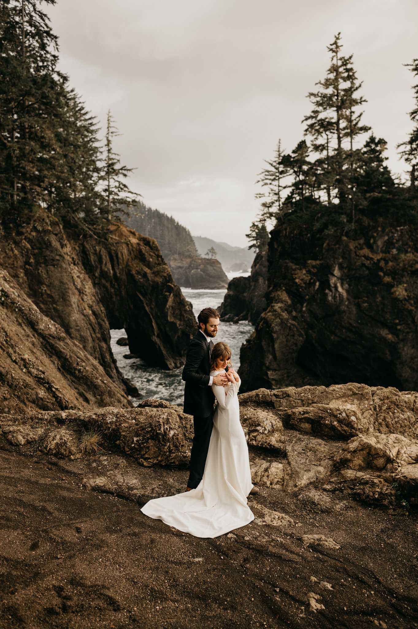 Bride and groom in wedding attire above the ocean after wedding ceremony in Oregon.