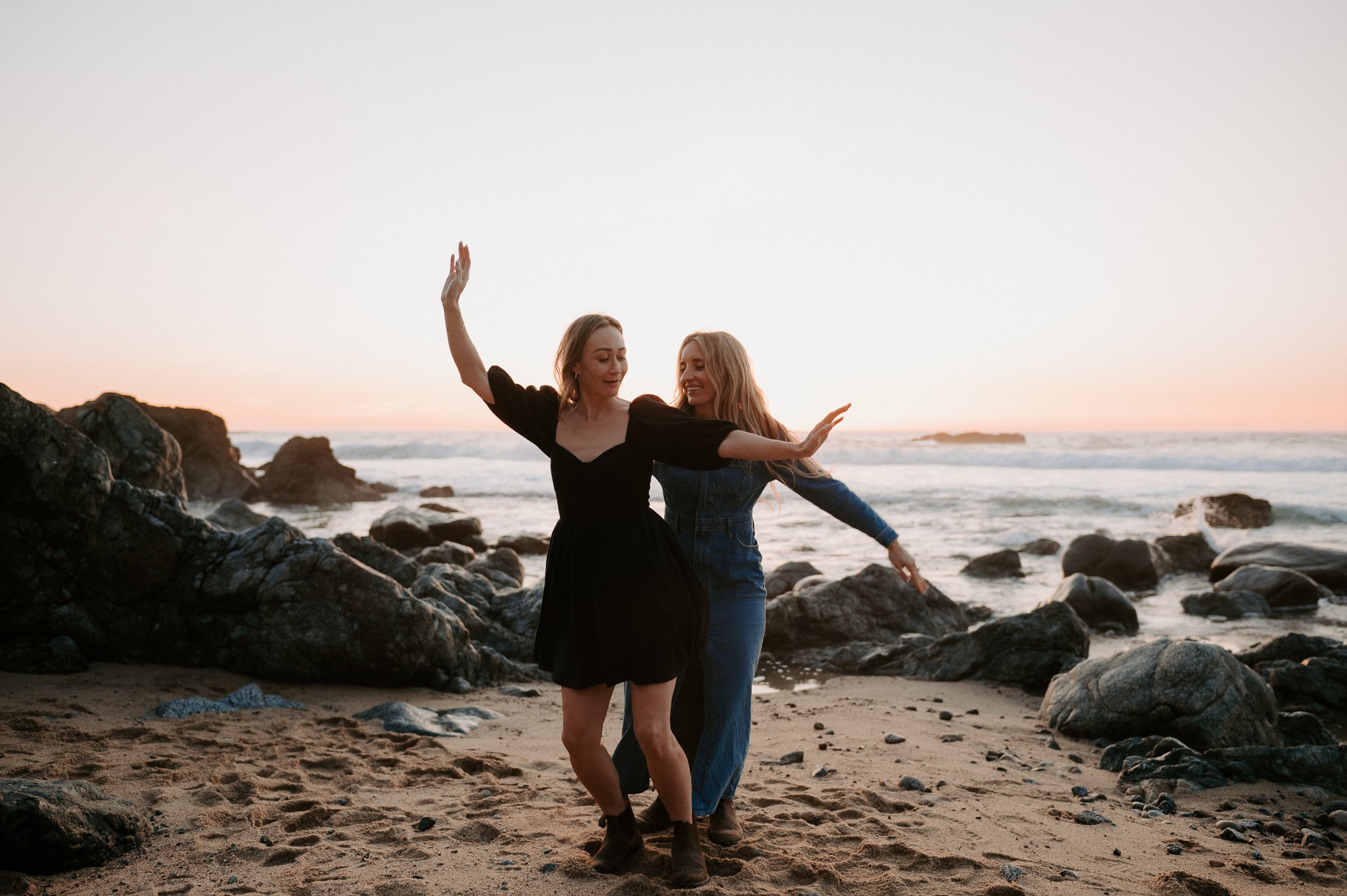  Newly engaged couple LGBTQ  dancing on rocks in the sunset in Big Sur California 