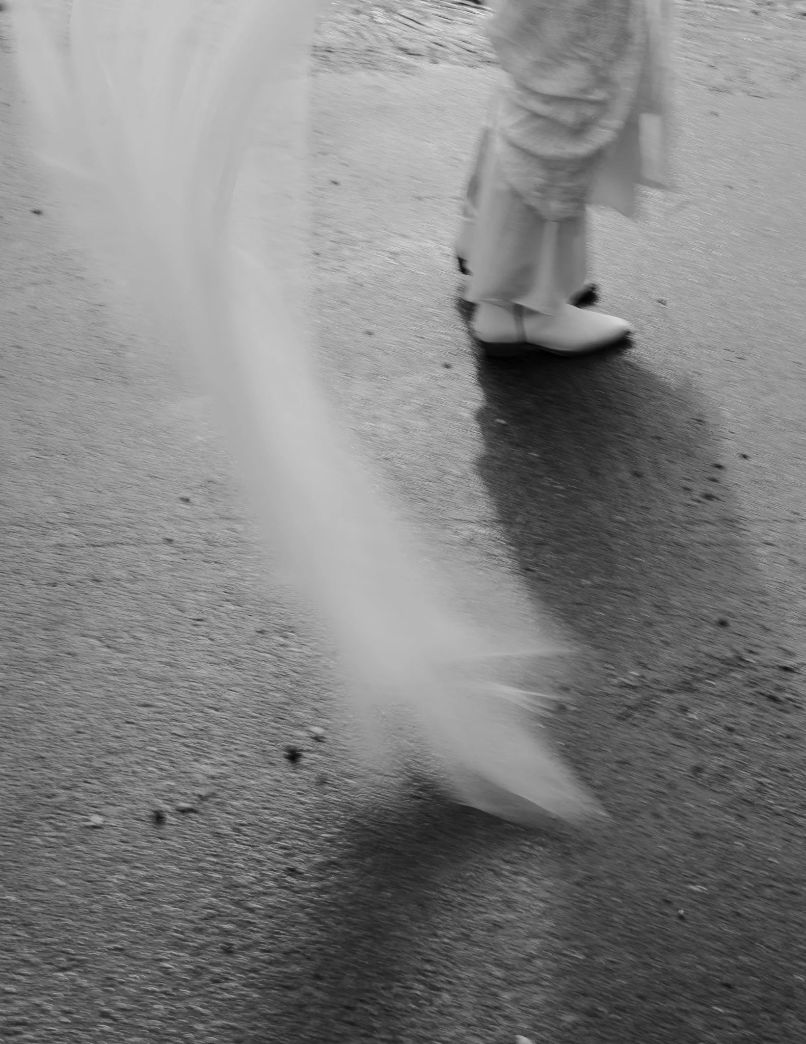 A person wearing cowboy boots and pants standing on a wet pavement near a water fountain.