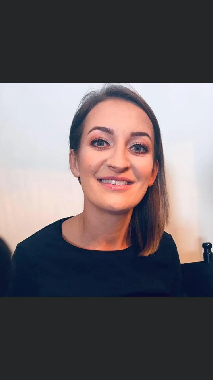 Portrait of a person smiling with short brown hair wearing a black top.
