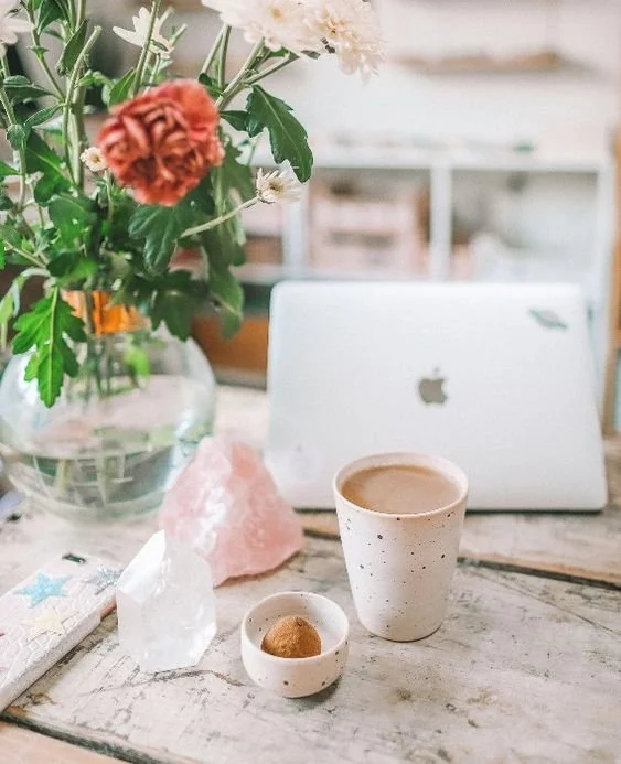 Cozy workspace with laptop, flowers, coffee, and crystals on wooden table