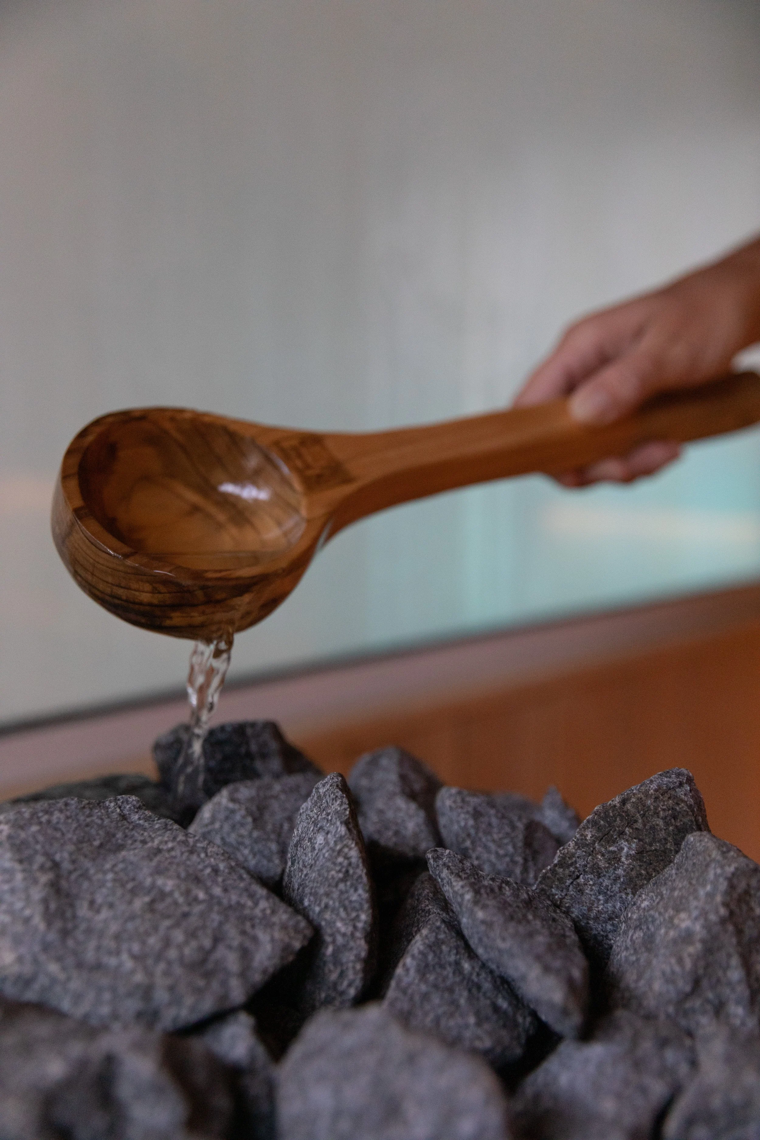 A wooden spoon pouring water onto hot rocks in the sauna.