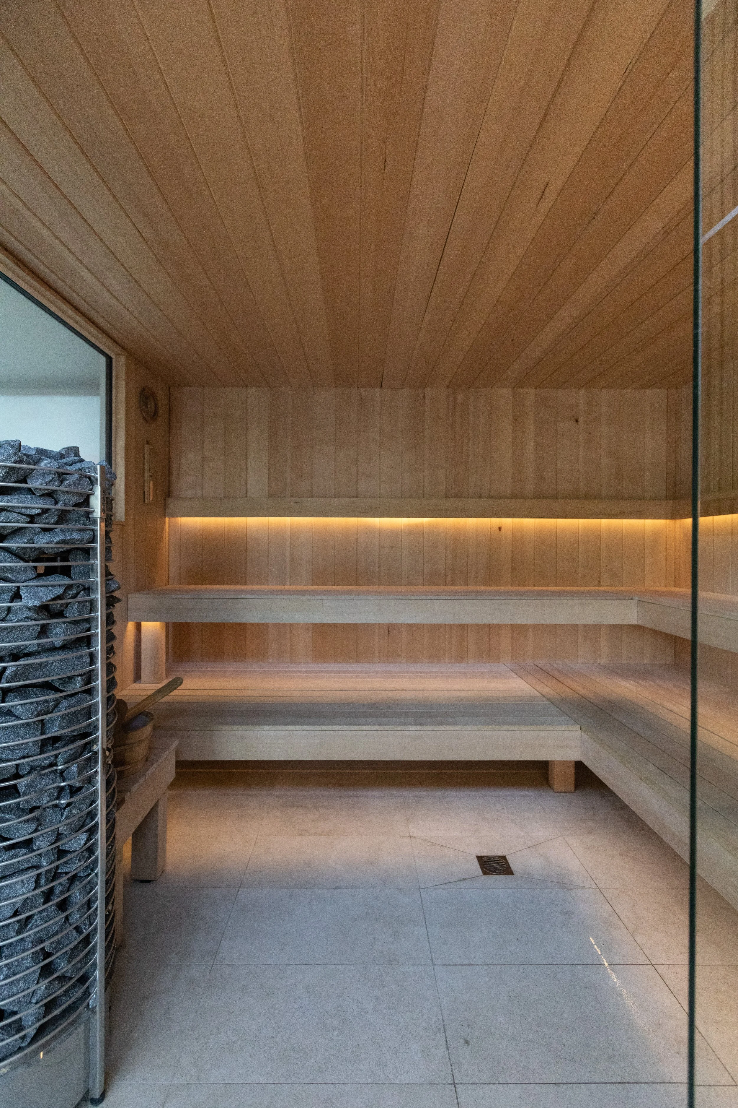 Interior of a wooden sauna with a bench, a wooden wall, and a glass door.