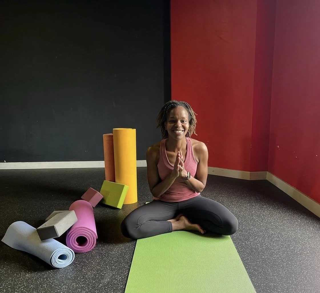Tabitha, a local yoga teacher in Emsworth, seated on a Yoga mat in Anjali Mudra surrounded by props.