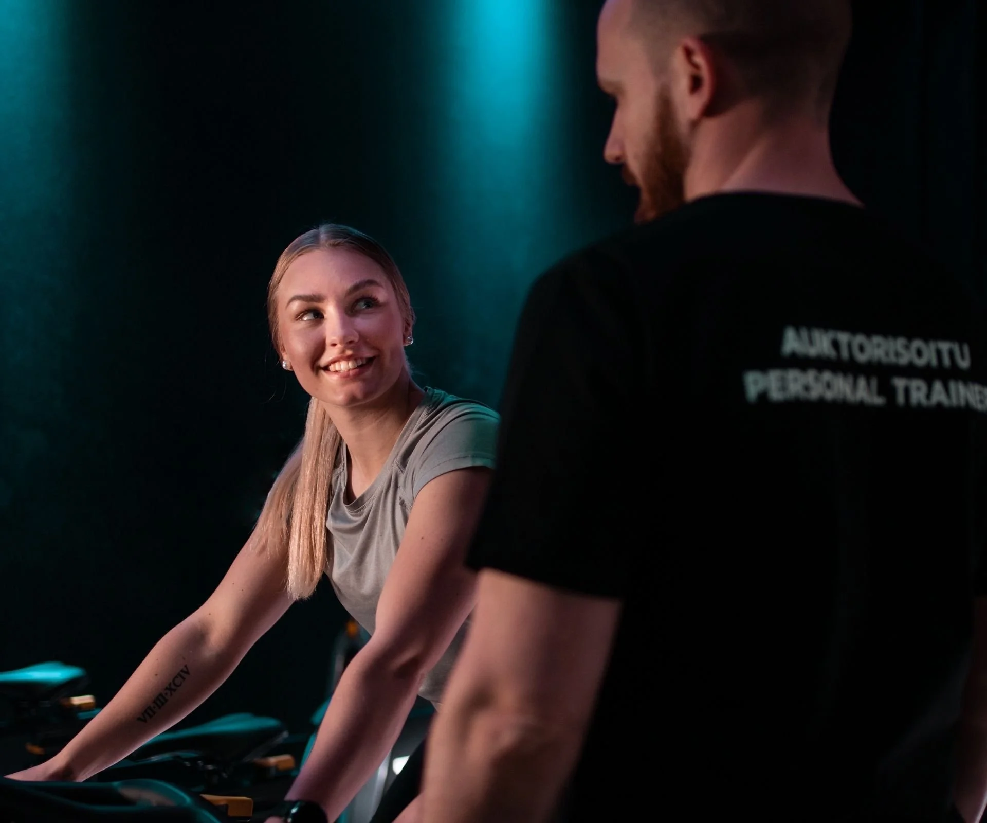 Nainen pyöräilee kuntosalilla ja keskustelee henkilökohtaisen valmentajan kanssa.