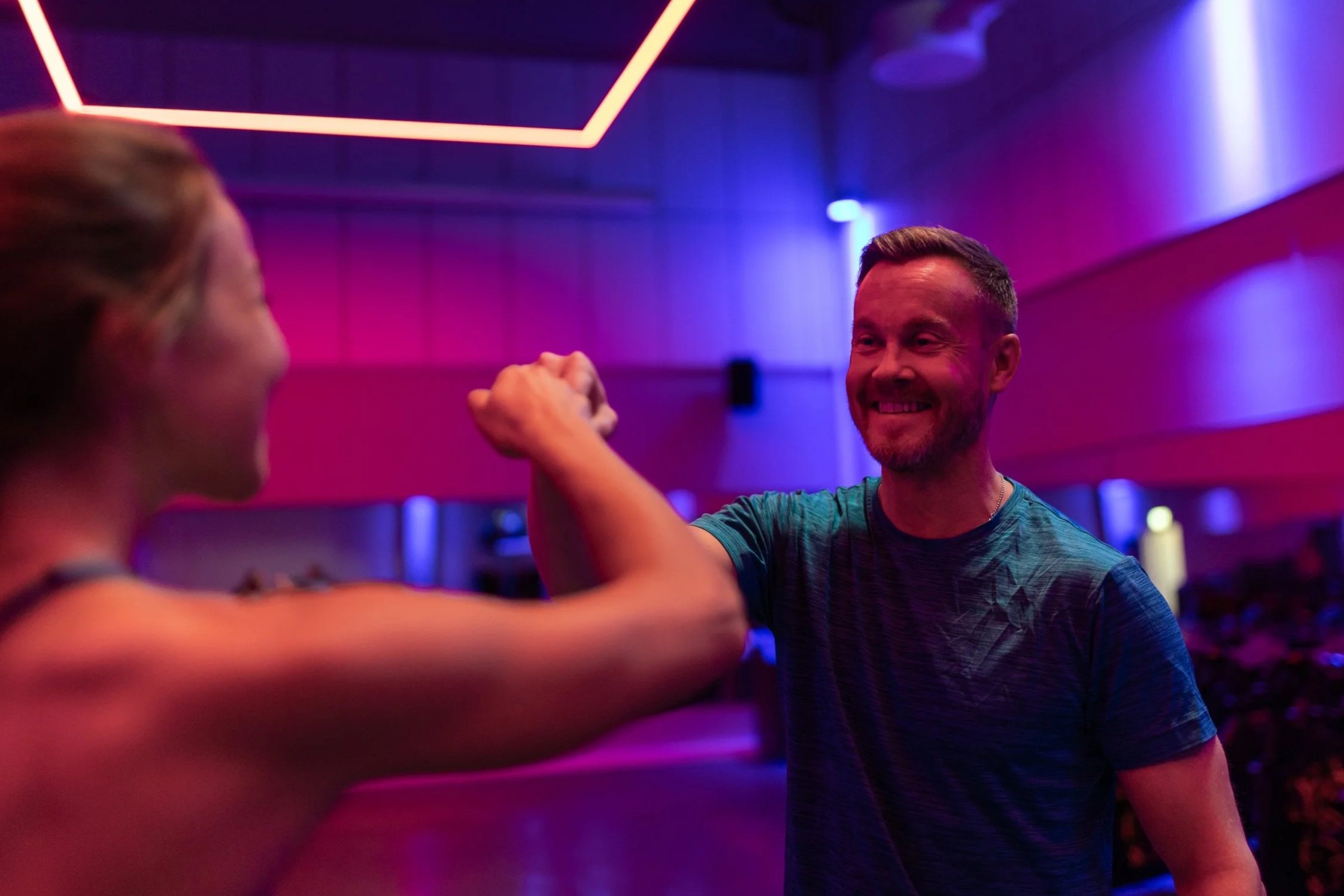 Kaksi liikunta-alan ammattilaista hymyilee ryhmäliikuntasalissa