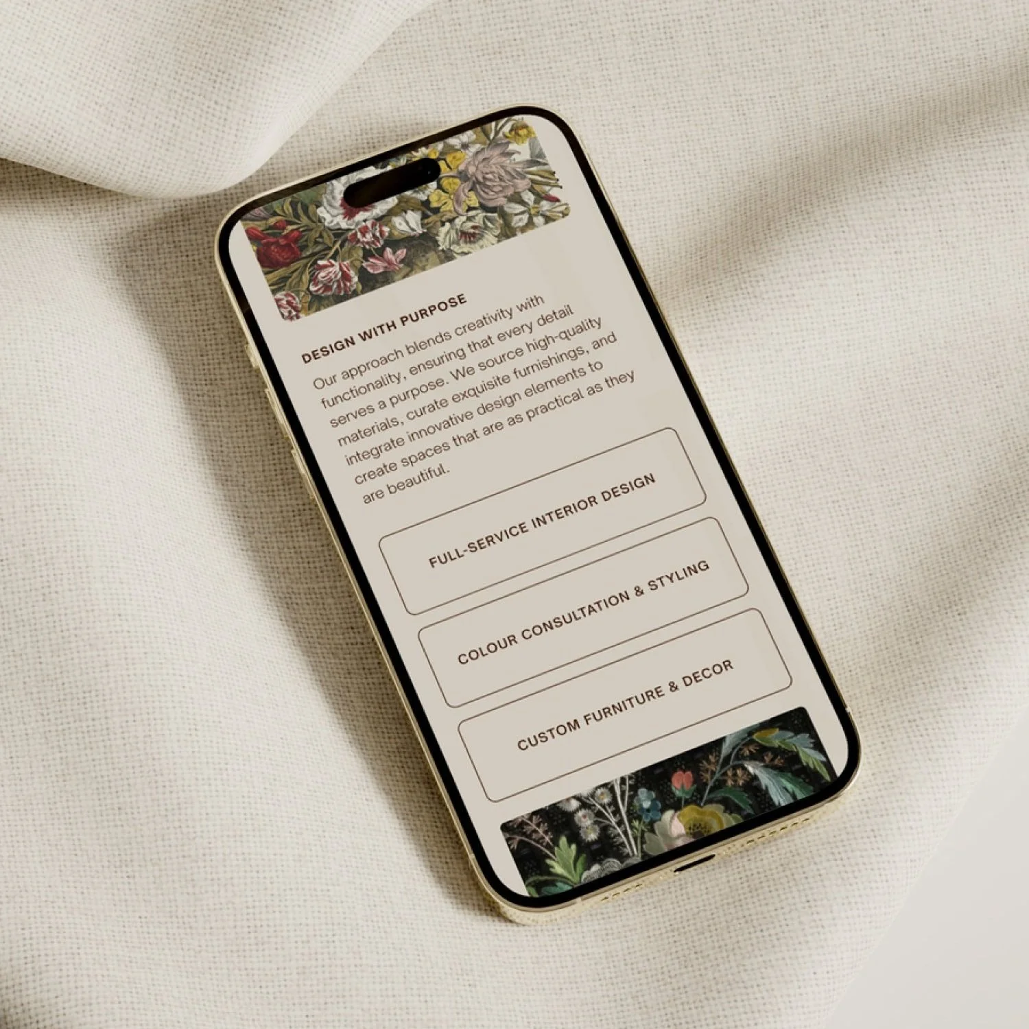 Smartphone with a floral header displaying interior design services list, placed on a white textured fabric background.