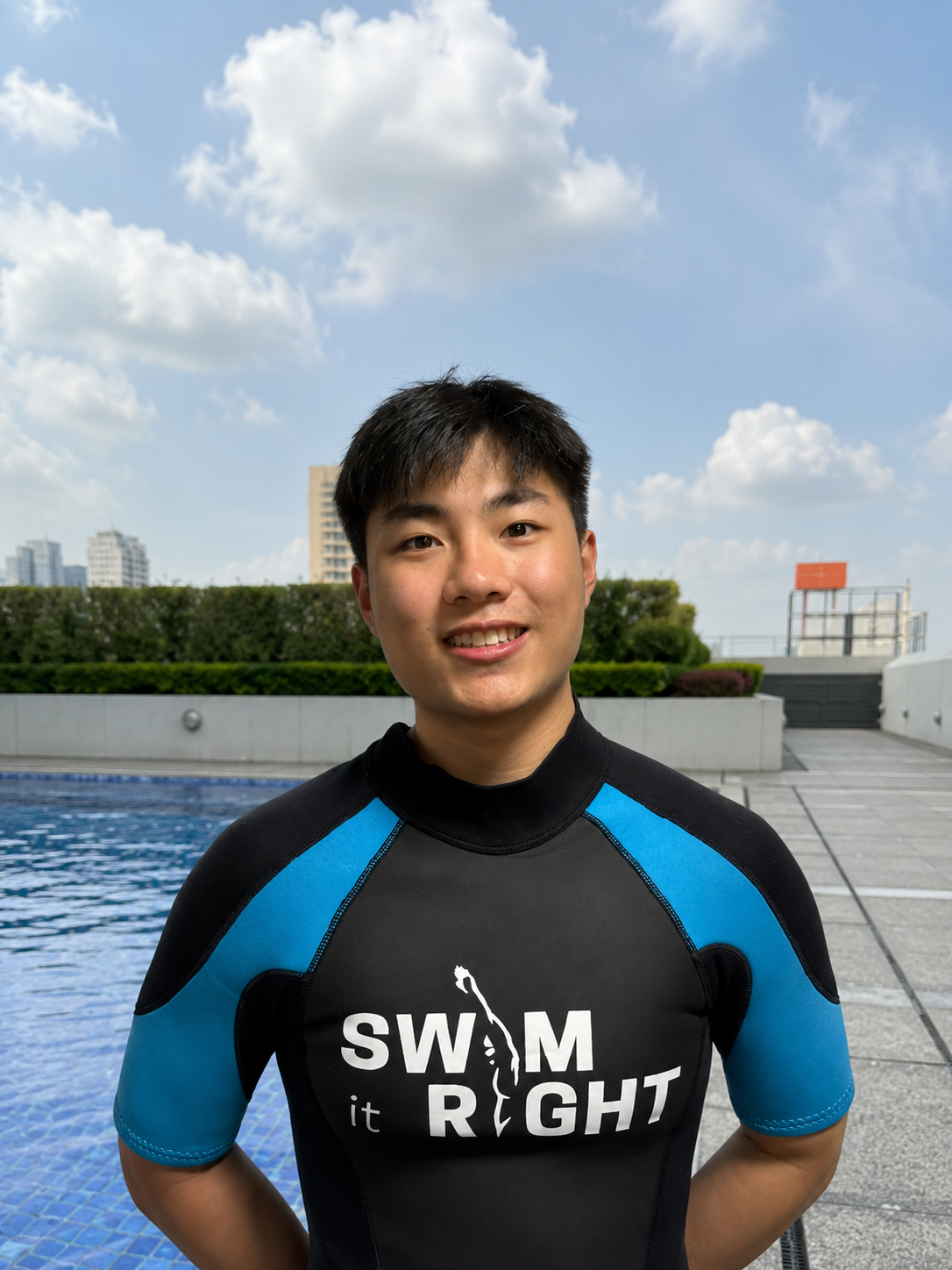 Young man in a navy and blue swim rash guard with the words 'SWIM it RIGHT' printed on the front, smiling at the camera.