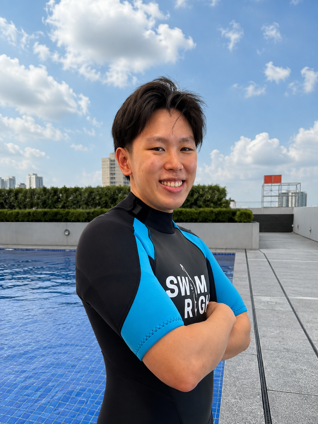 Young man in a black and blue swim shirt smiling with arms crossed against a plain white background.