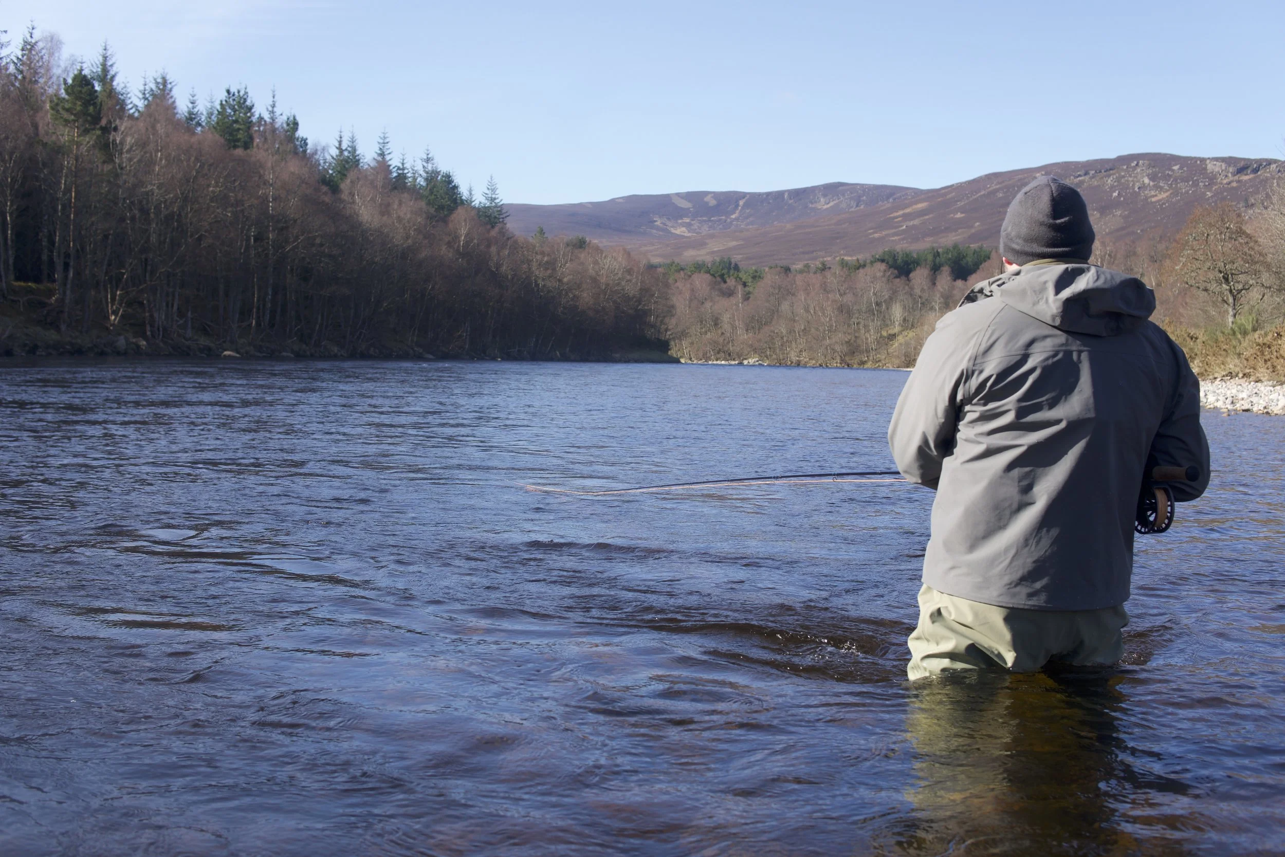 Angler wading in the River Dee, fly fishing on a bright summer day