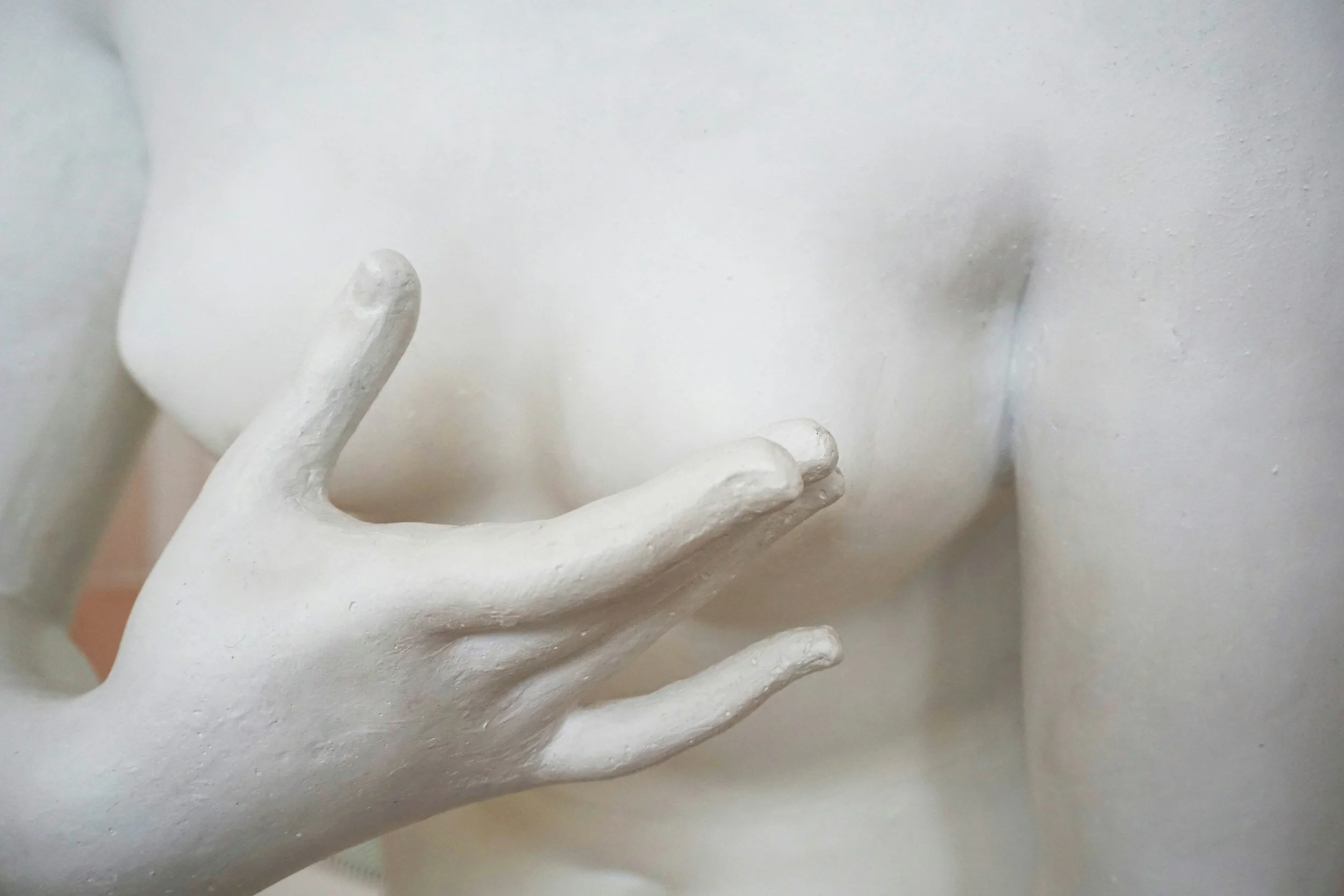 Close-up of a white marble statue's hand and upper body, focusing on the hand near the chest.