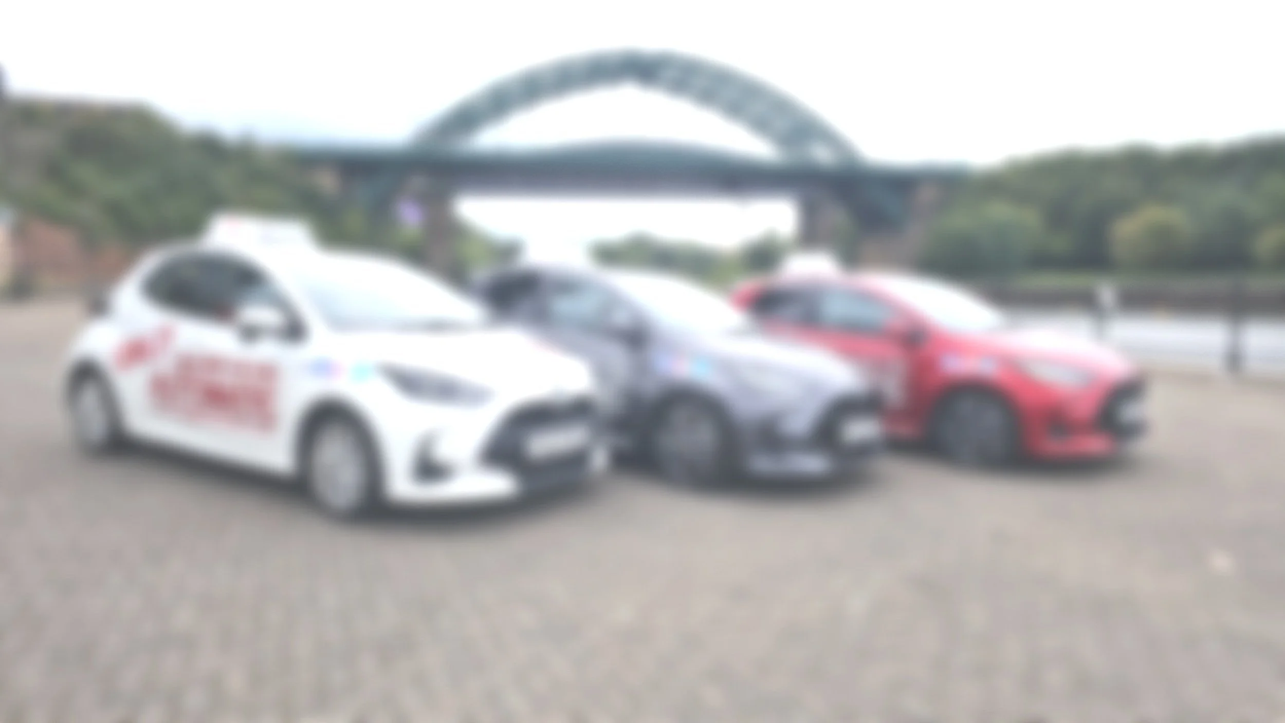 Three parked cars with a bridge in the background, out of focus