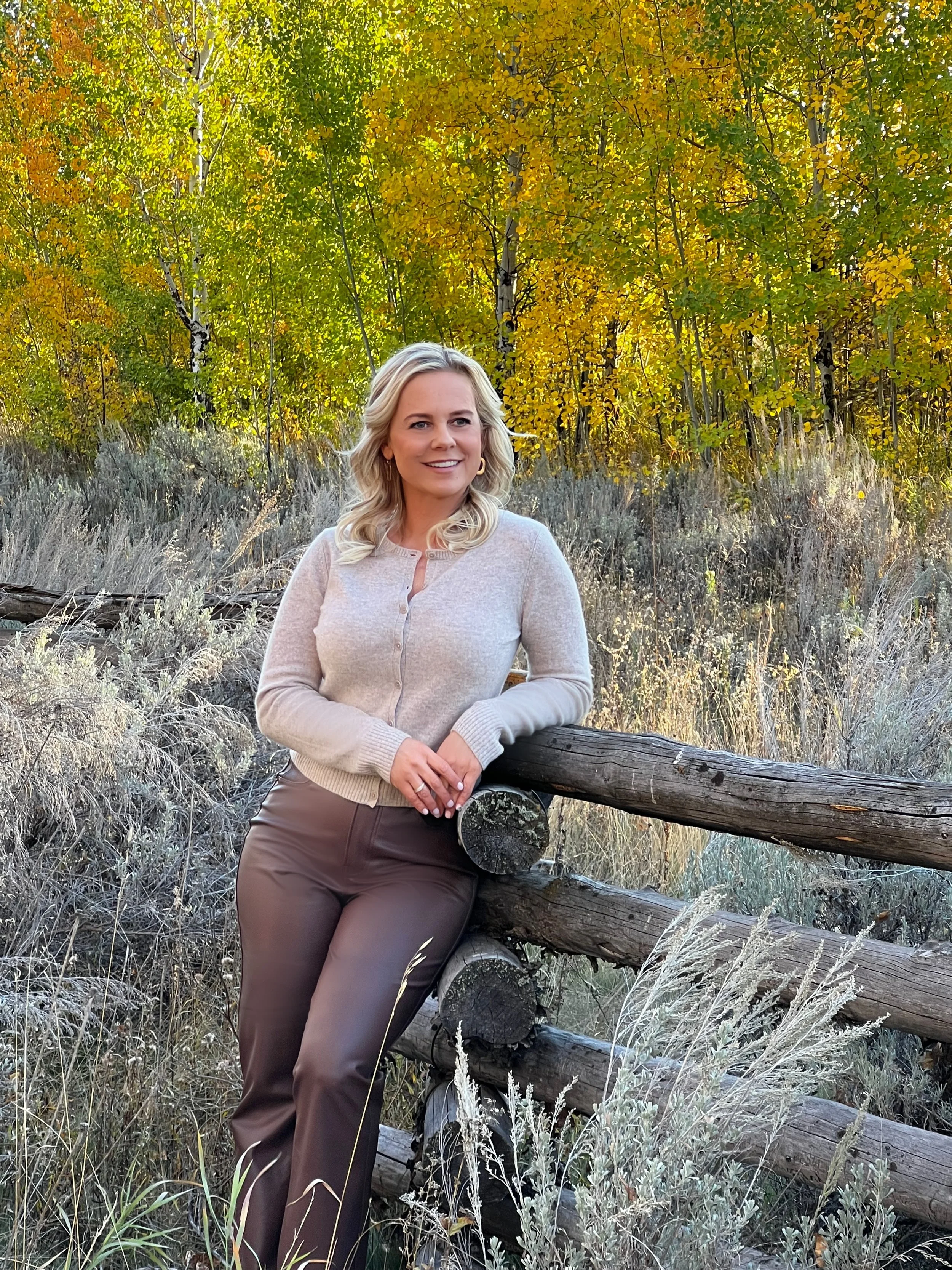 Patricia Kennedy, founder of Rendezvous Design, leaning on a rustic wooden fence among golden autumn aspens