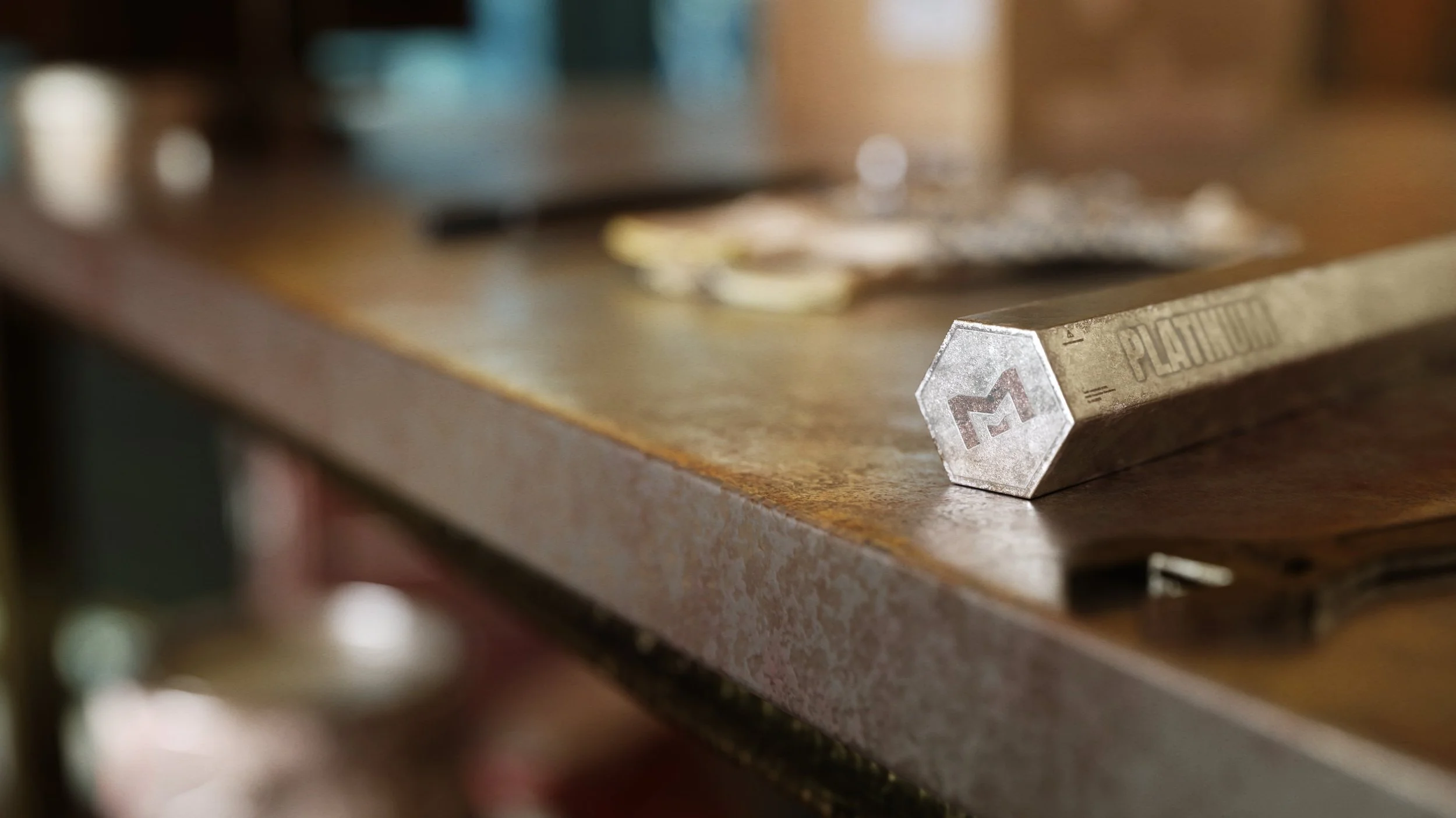 Close-up of a metal tool or object labeled 'PLASTIC' and 'M', resting on a wooden workbench in a workshop setting.