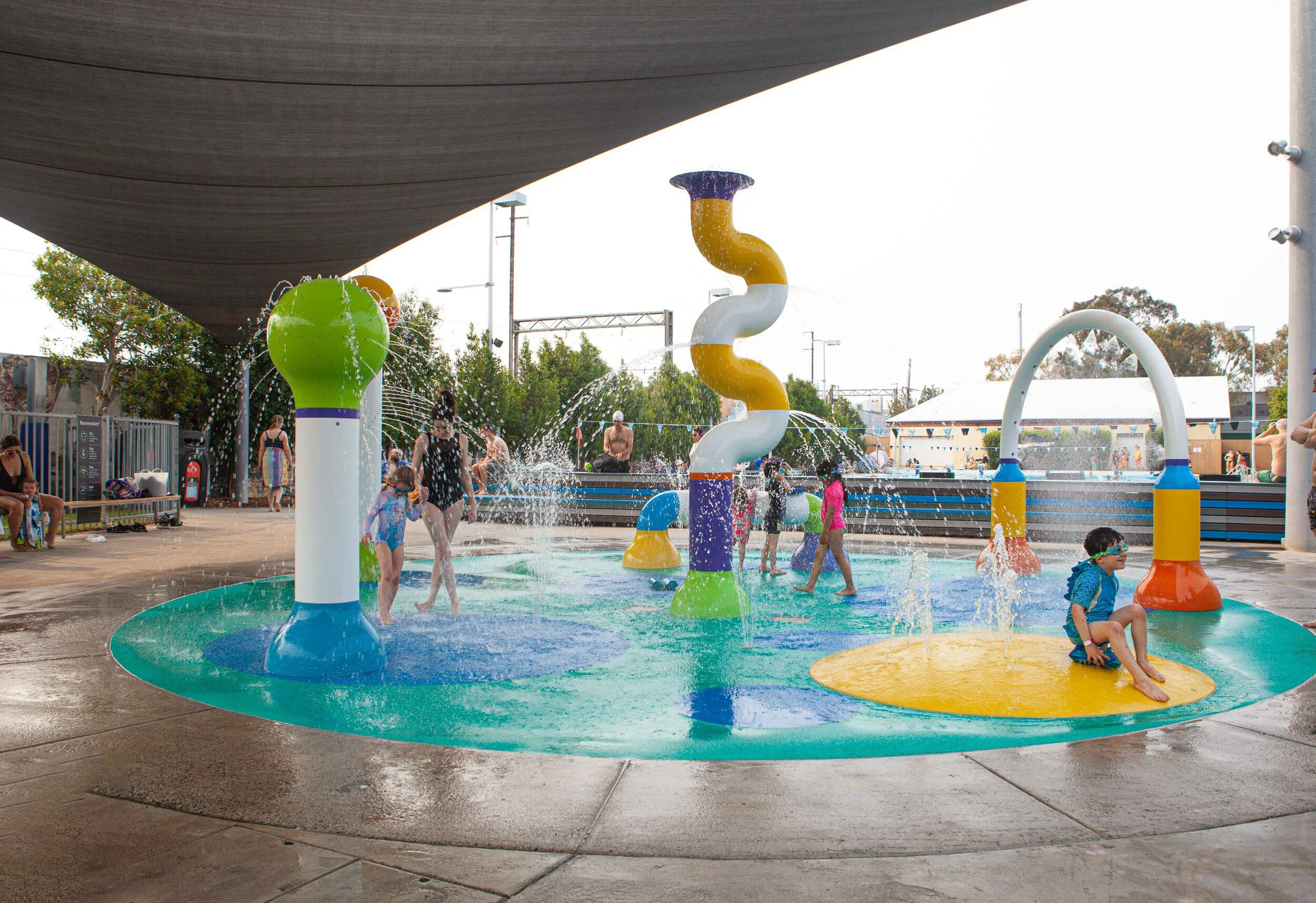 Children playing on colorful water play area with fountains and slides at an outdoor water park in the daytime.
