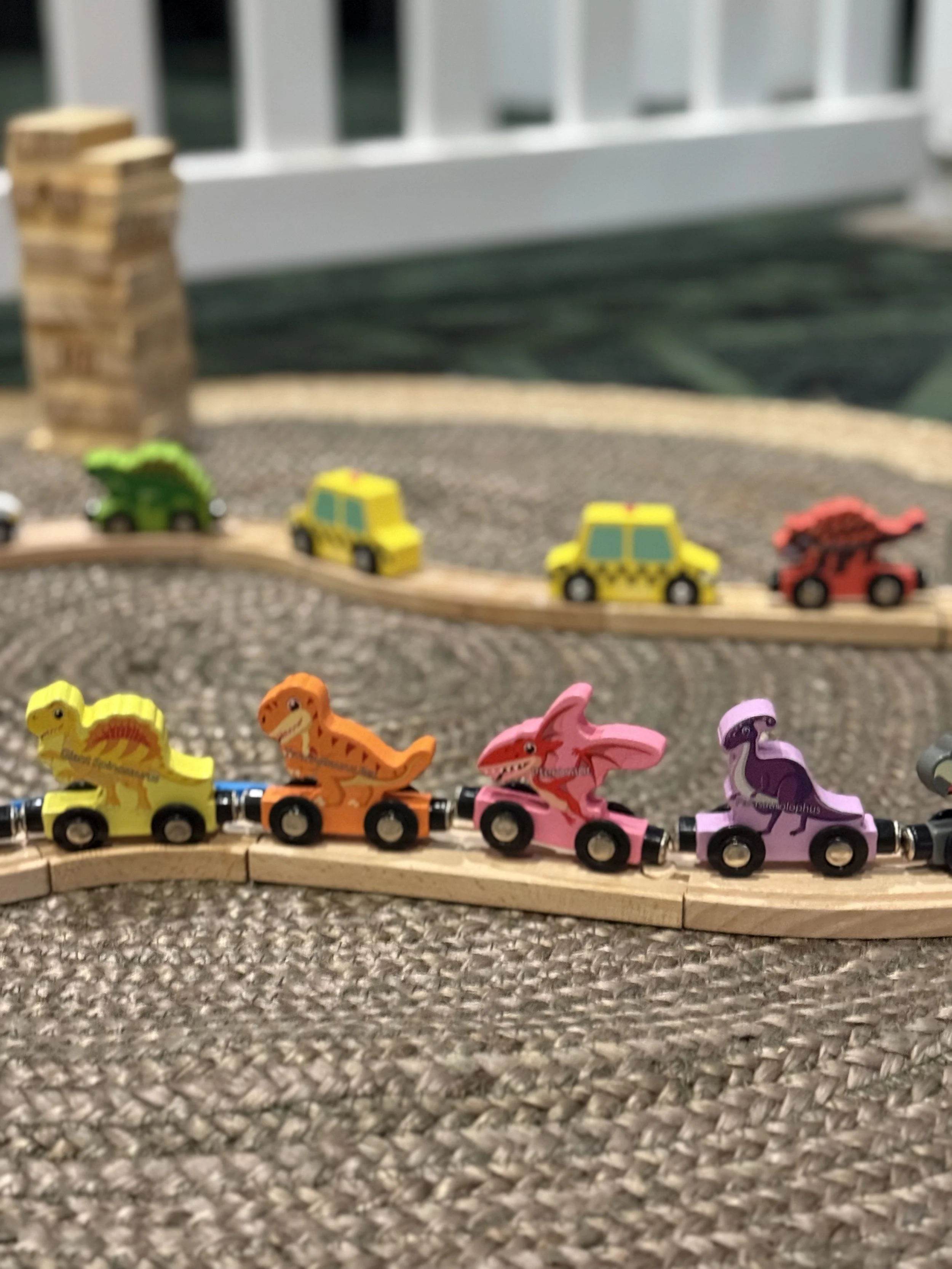 Colorful toy dinosaur and vehicle toys on a wooden train track.