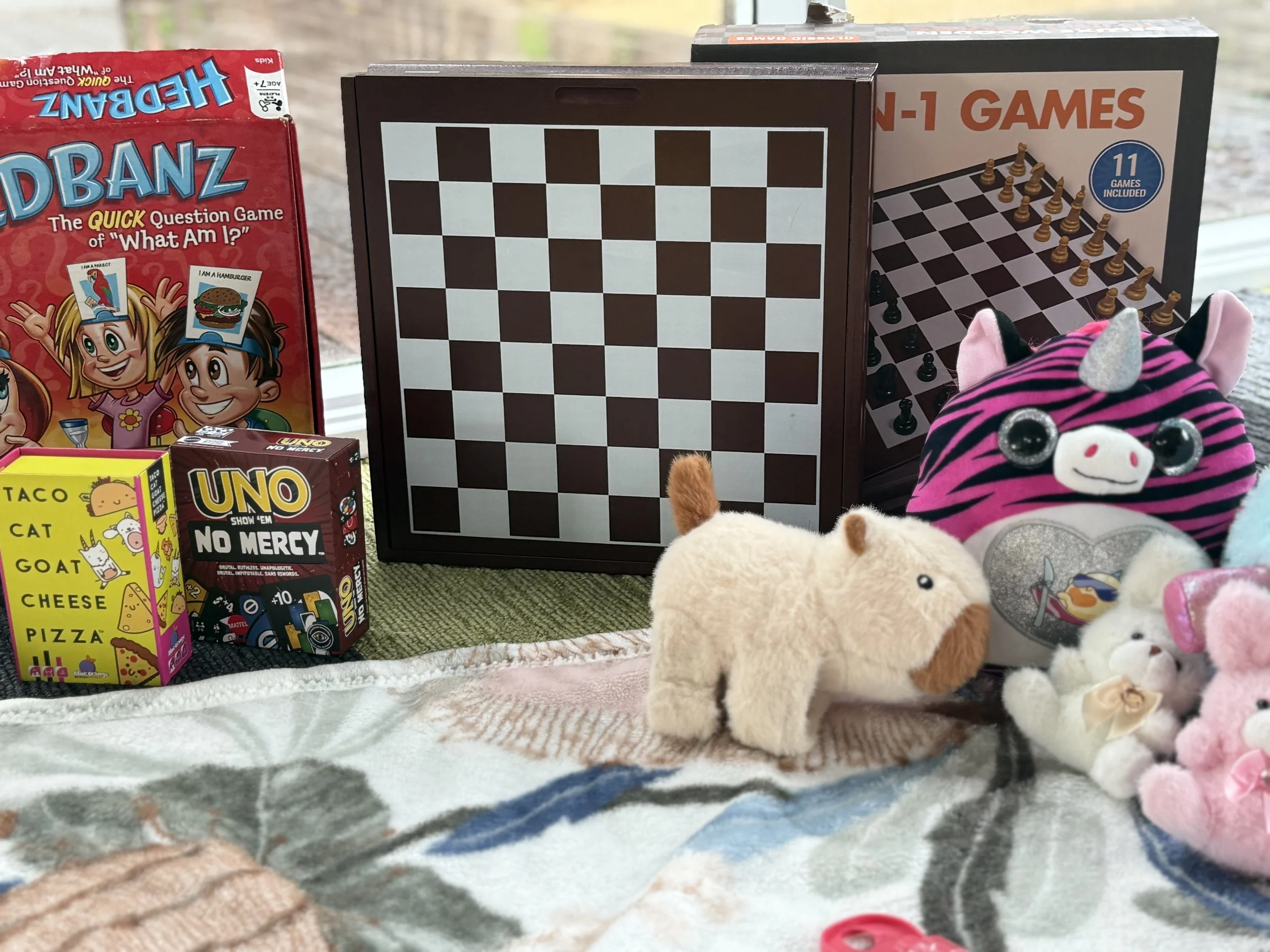 Collection of board games, plush toys, and a chessboard set on a table.