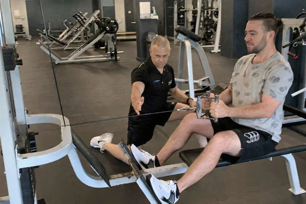 Warren Manson coaching a client on proper seated cable row technique during a personal training session