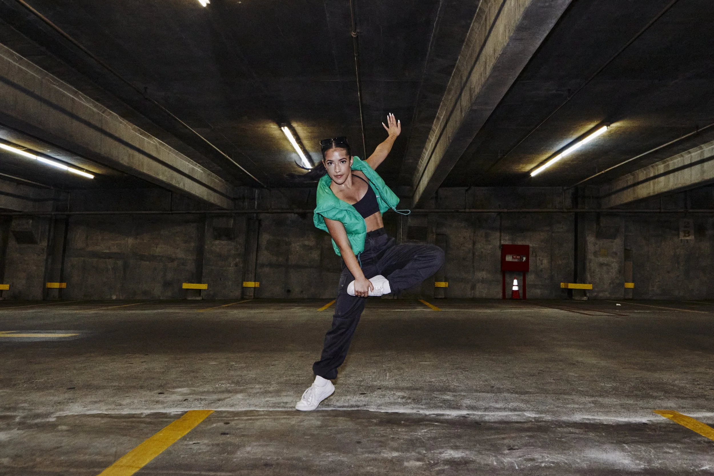 A woman dancing in an empty parking garage with concrete walls and yellow parking space lines.