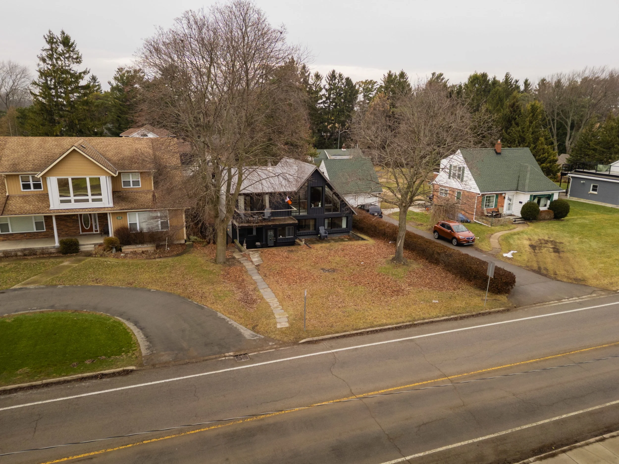 Aerial view of a residential neighborhood showing multiple houses, trees, a parked car, and a street with yellow lines.