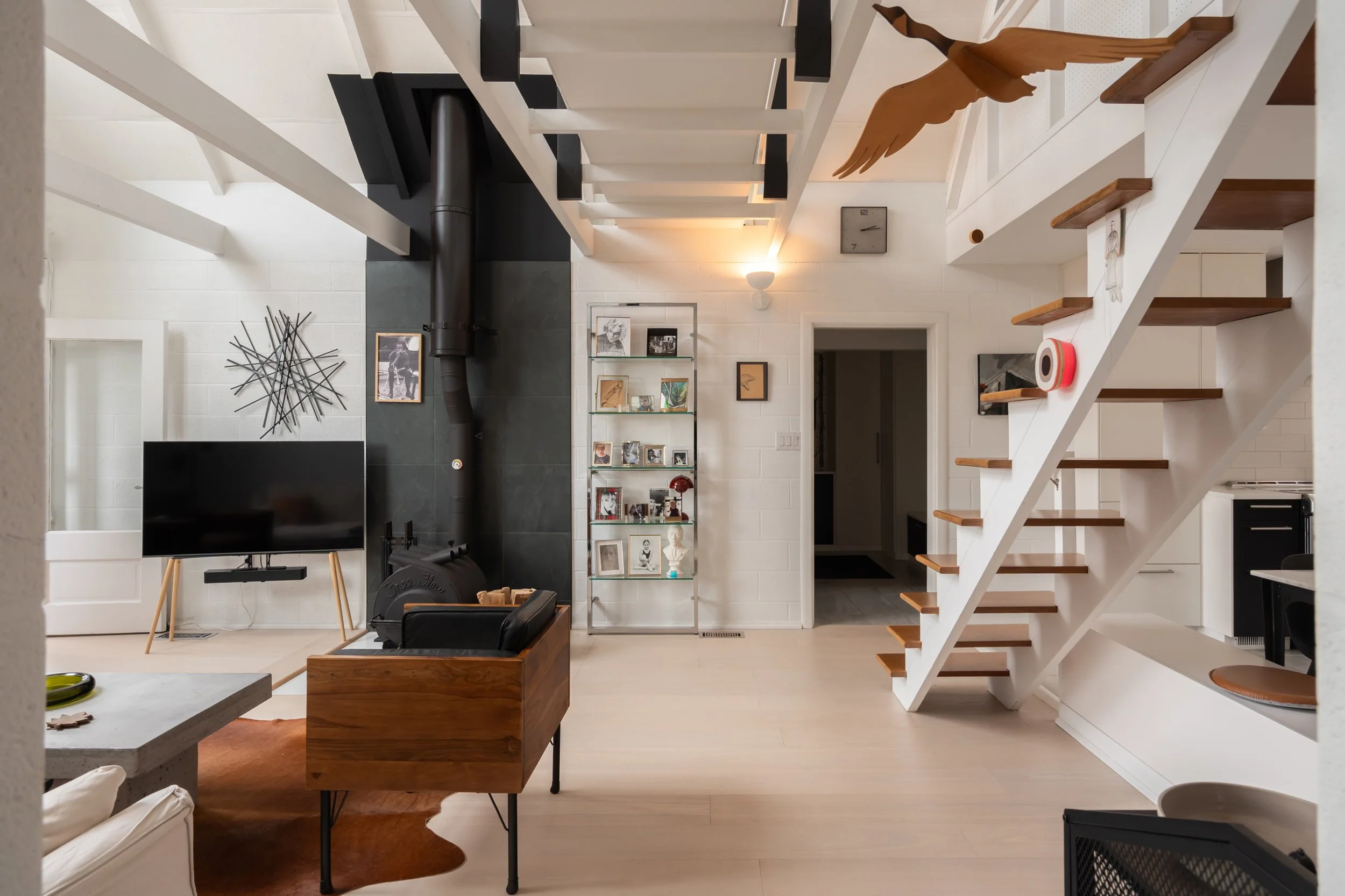 A cozy living room with a white staircase, a mounted TV, a black fireplace, a bookshelf, and various decorative items on the walls and shelves.