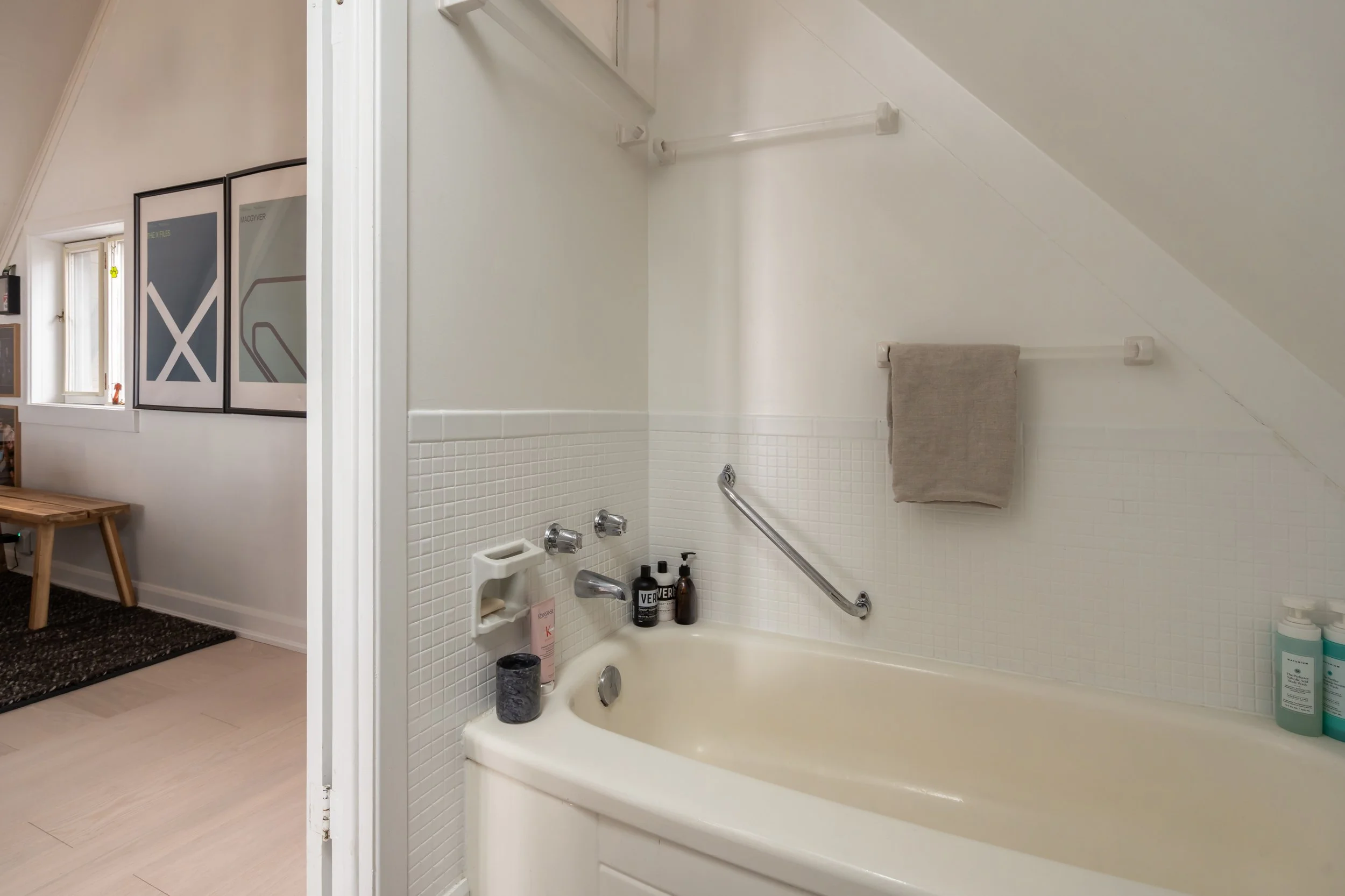 Bathroom with a bathtub, a beige towel, and toiletries on the edge of the tub.