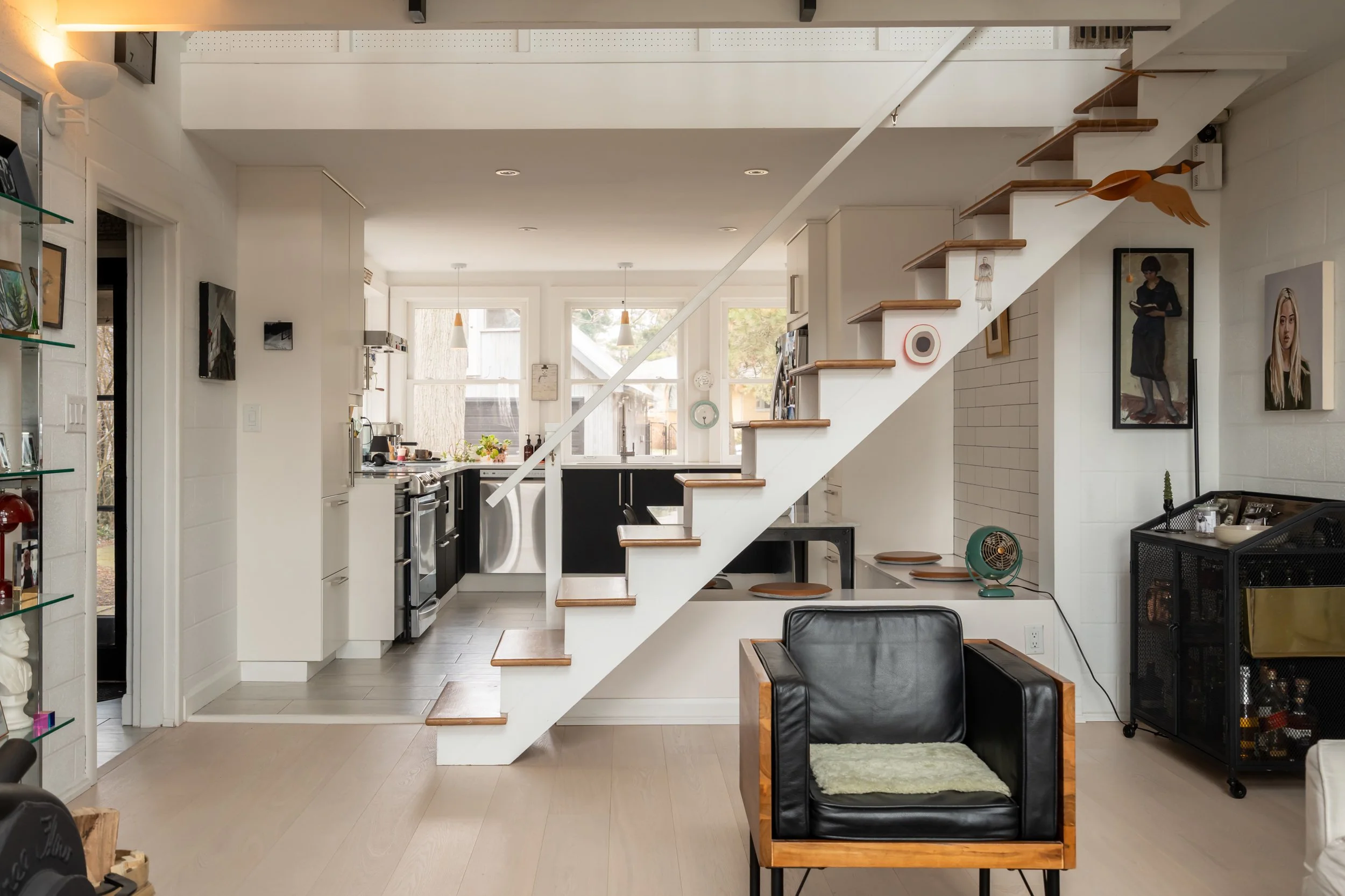 Interior of a modern home featuring a staircase, black and white kitchen, and a sitting area with a black leather chair.