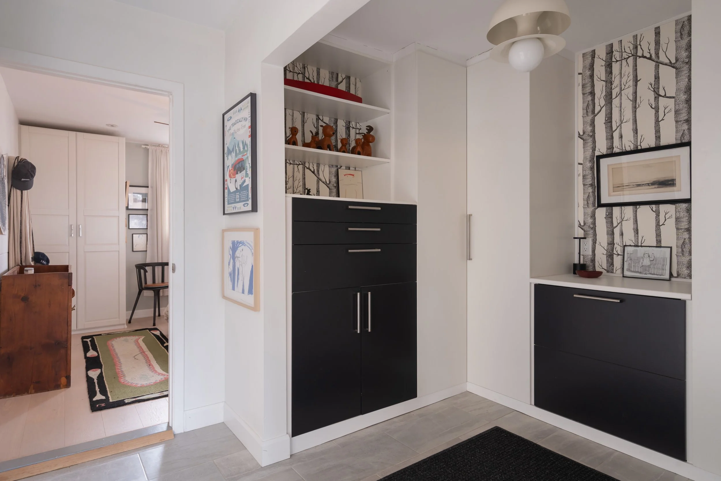 Interior of a home with a white and black color scheme, featuring built-in cabinets, decorative art, and patterned wallpaper resembling trees.