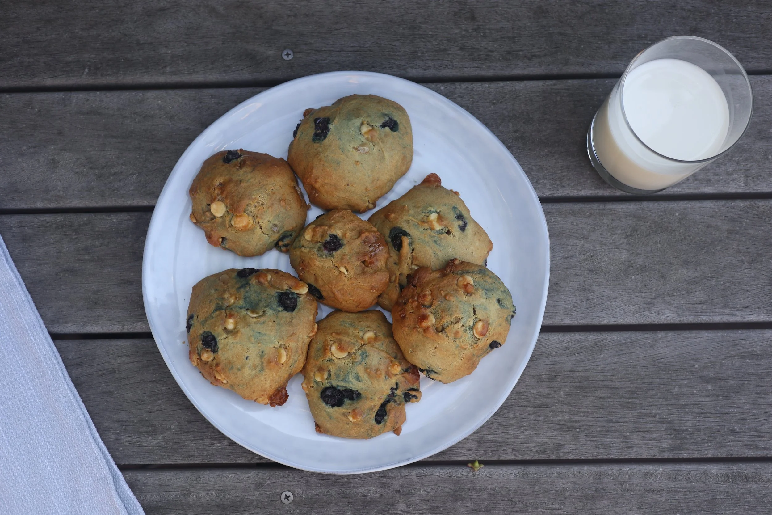 Blueberry white chocolate chip cookies on a blue plate with a glass of milk next to them. The cookies are low-histamine, which is good for those who have MCAS.