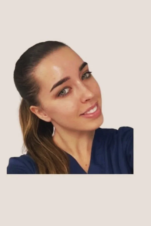 A young woman with light brown hair tied back, wearing a dark blue top, smiling with a white background.