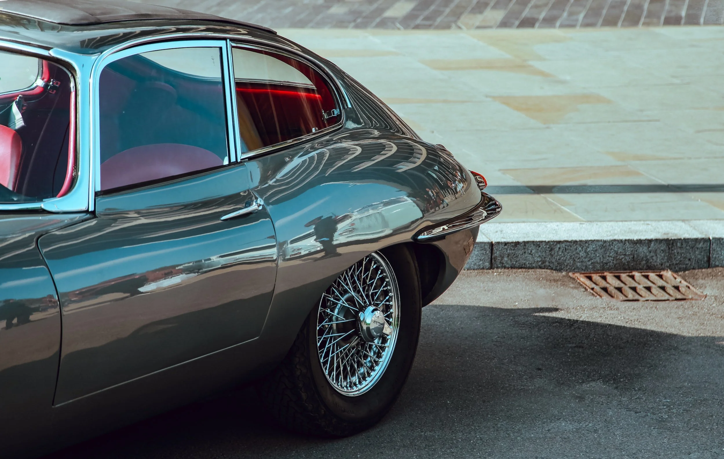Close-up of a vintage black car with chrome wire wheels parked on the street, reflecting the sky and surroundings.