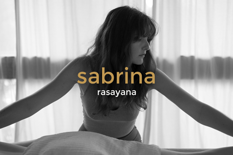 Black and white photo of a woman with long hair stretching on a bed with curtains in the background, overlaid with the text 'sabrina rasayana'.