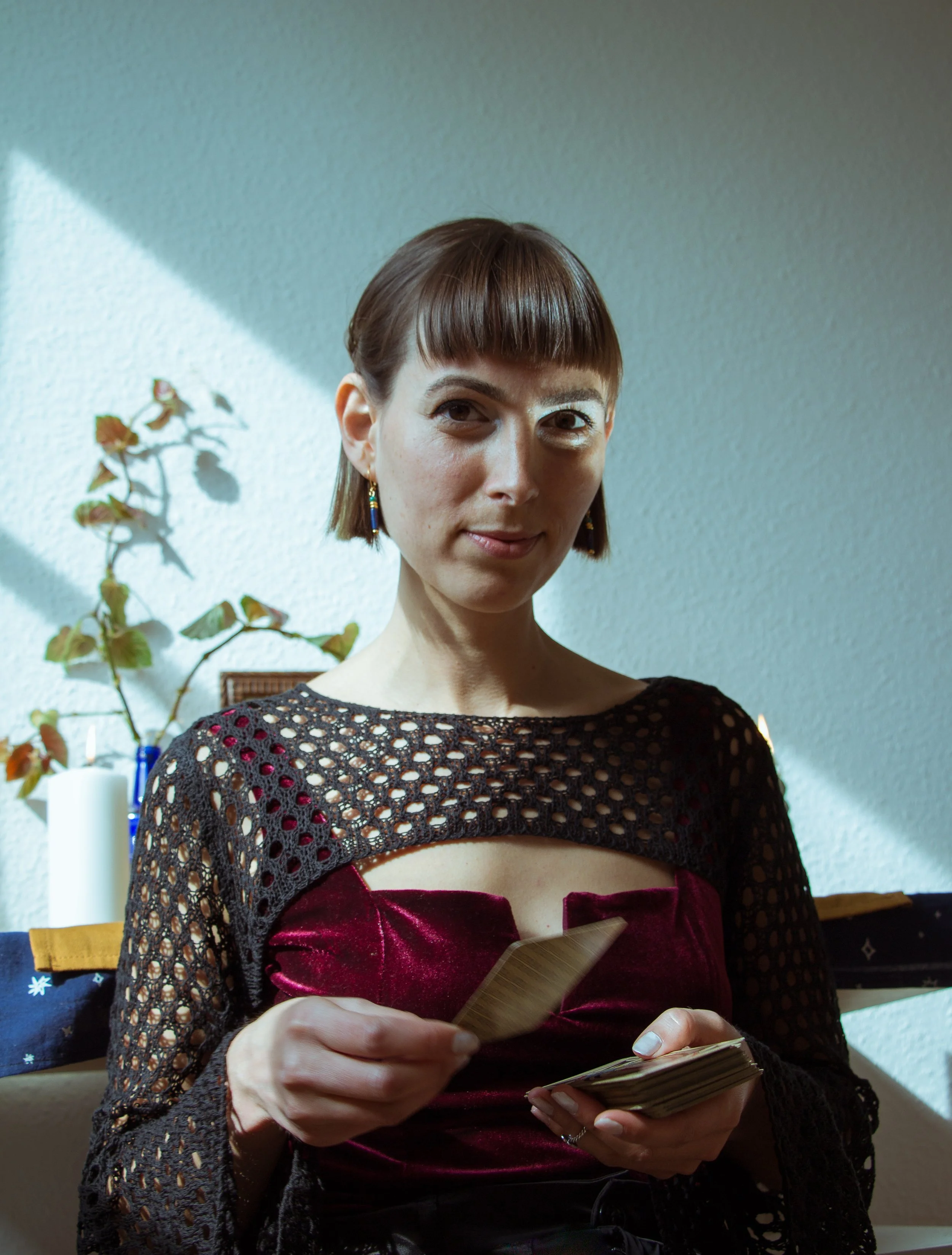 A woman with short brown hair and blue earrings holding a deck of tarot cards