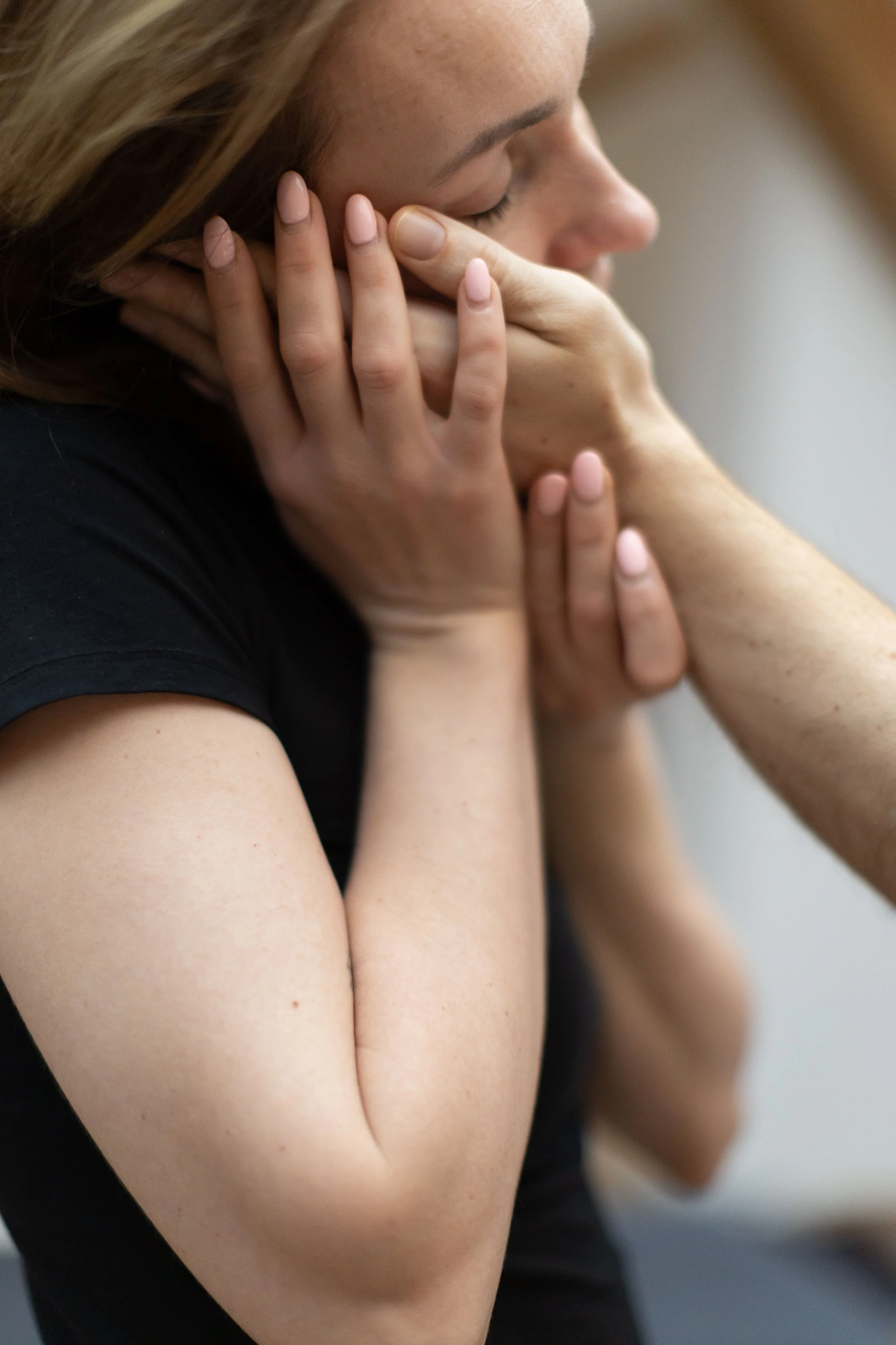 A woman with closed eyes embracing another person's arm with both hands.