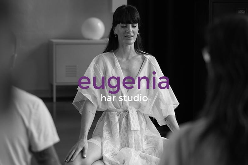 A woman dressed in a light, loose robe sitting cross-legged, with her eyes closed and a serene expression, in a studio setting with two other people partially visible. The text 'eugenia har studio' is overlaid on the image.