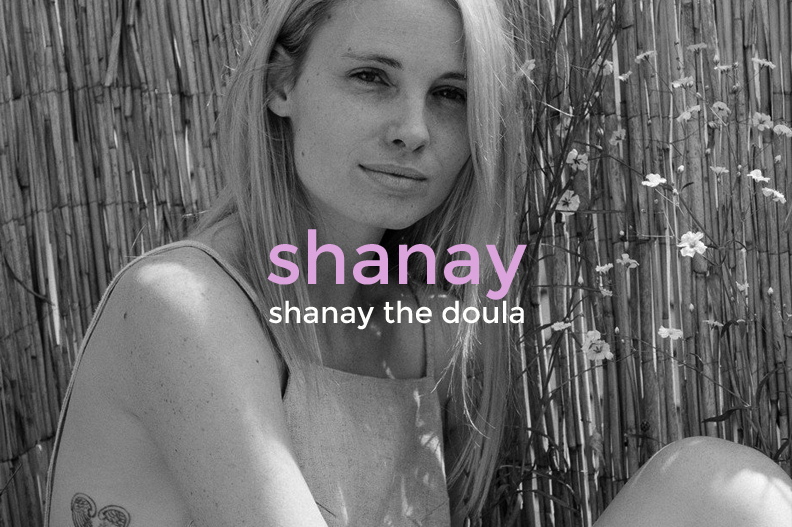 Black and white photo of a young woman with long blonde hair sitting outdoors near a bamboo fence and some flowers, with text overlay that reads 'shanay shanay the doula' in pink and white.