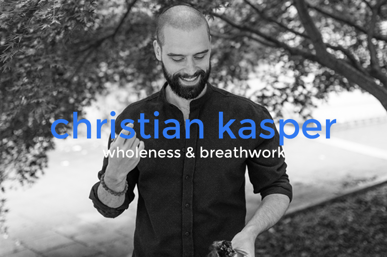 Black and white photo of a smiling man with a beard looking down, outdoors with trees in the background, holding a small object in his hand.