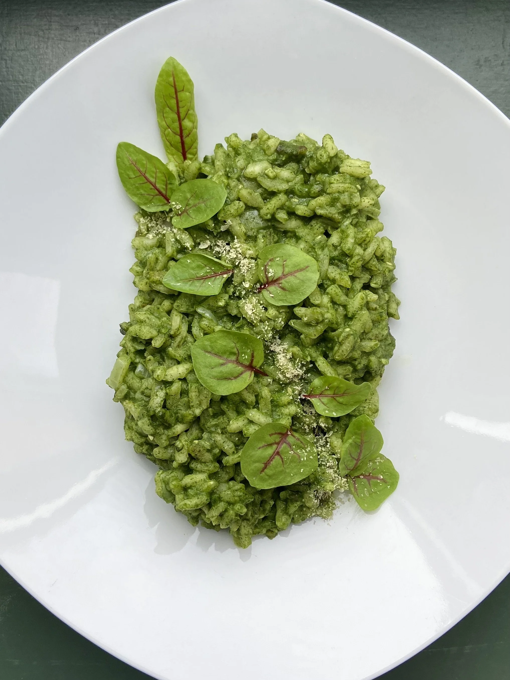 Green pasta dish garnished with microgreens and grated cheese on a white plate.