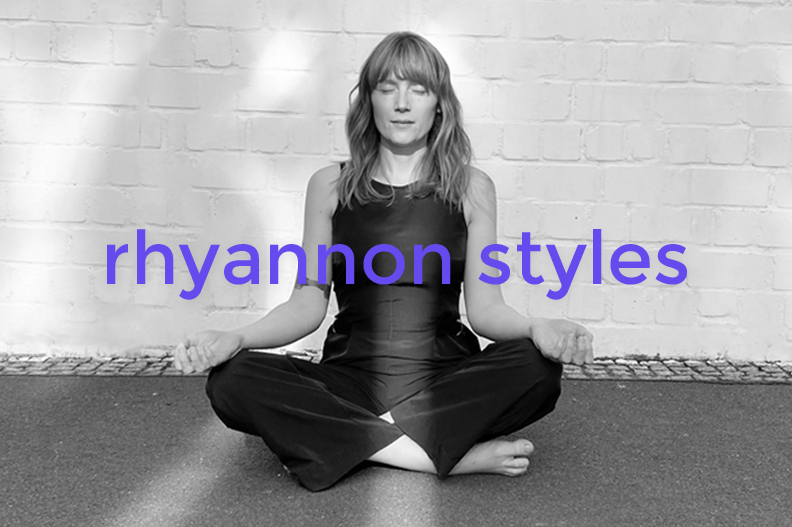 A woman practicing meditation in a seated lotus position against a brick wall, with the text 'rhyannon styles' overlaid.