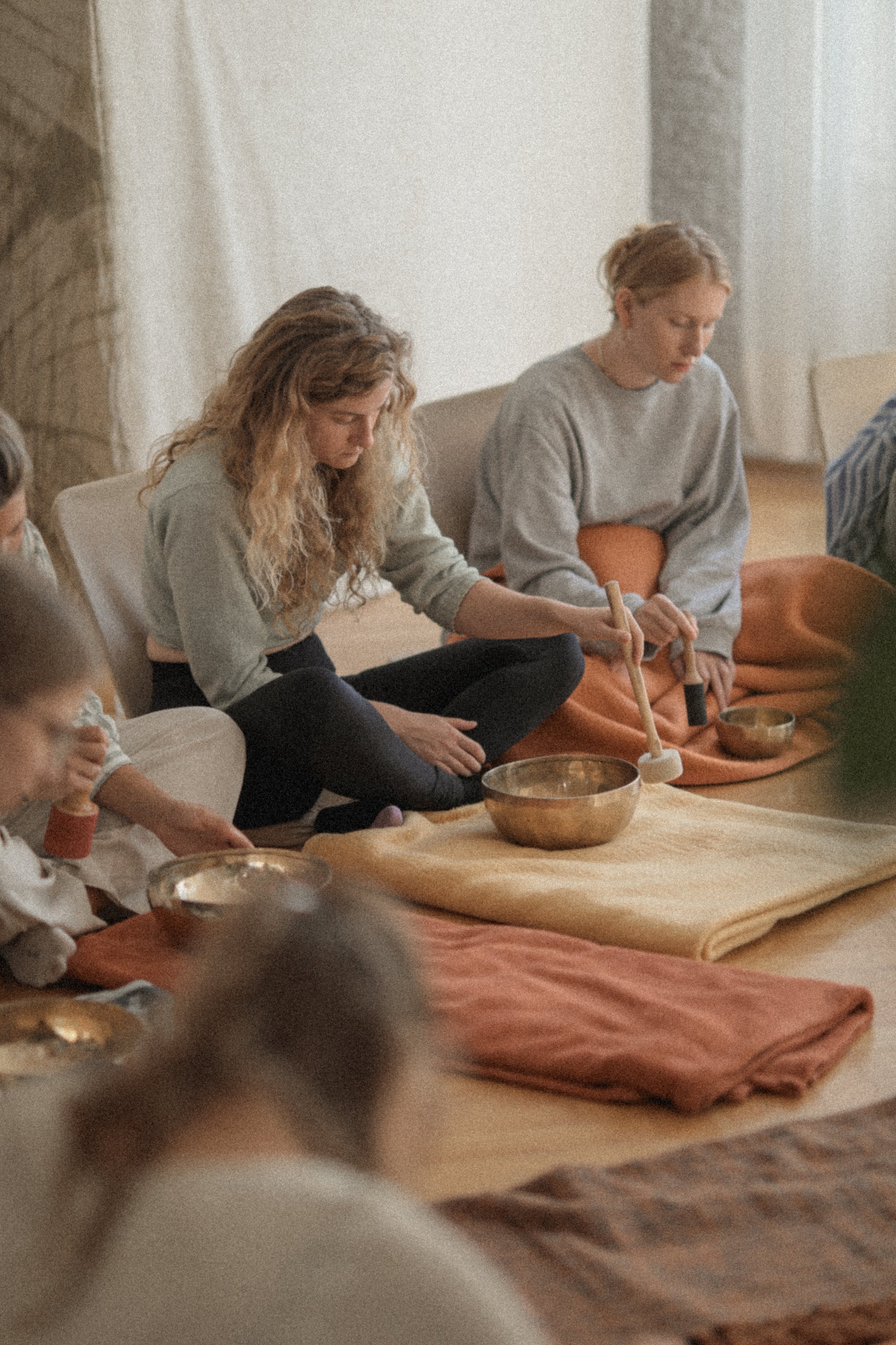 Women sitting on the floor participating in a meditation or sound healing session with singing bowls.
