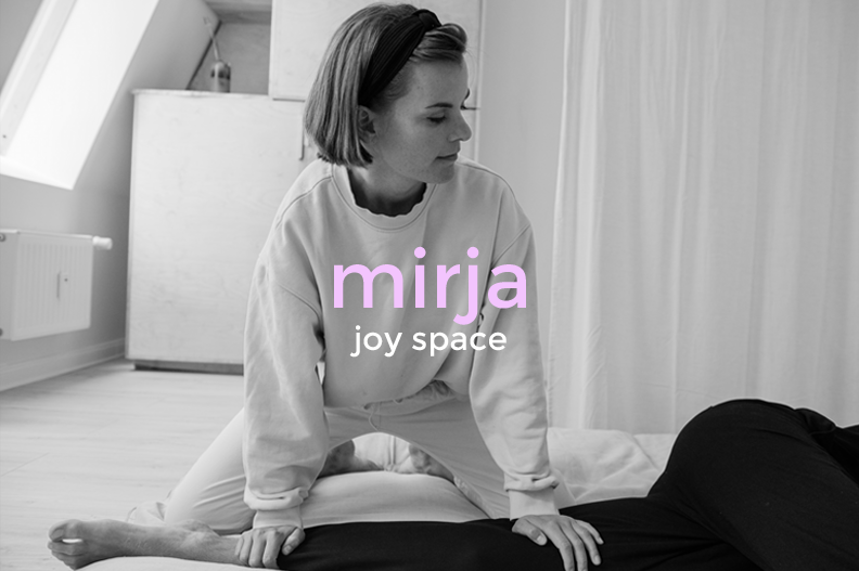 A woman performing a massage or stretching exercise on a person lying face down on a bed in a bright room with light-colored curtains.