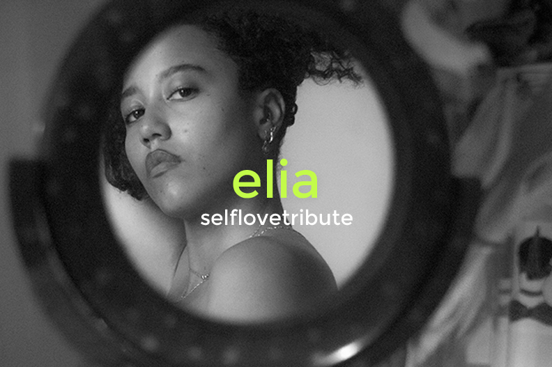 A black and white photo of a woman with short, curly hair, wearing earrings, looking at the camera through a round mirror or camera lens, with the text "elia selflovetribute" overlaid in green and white.