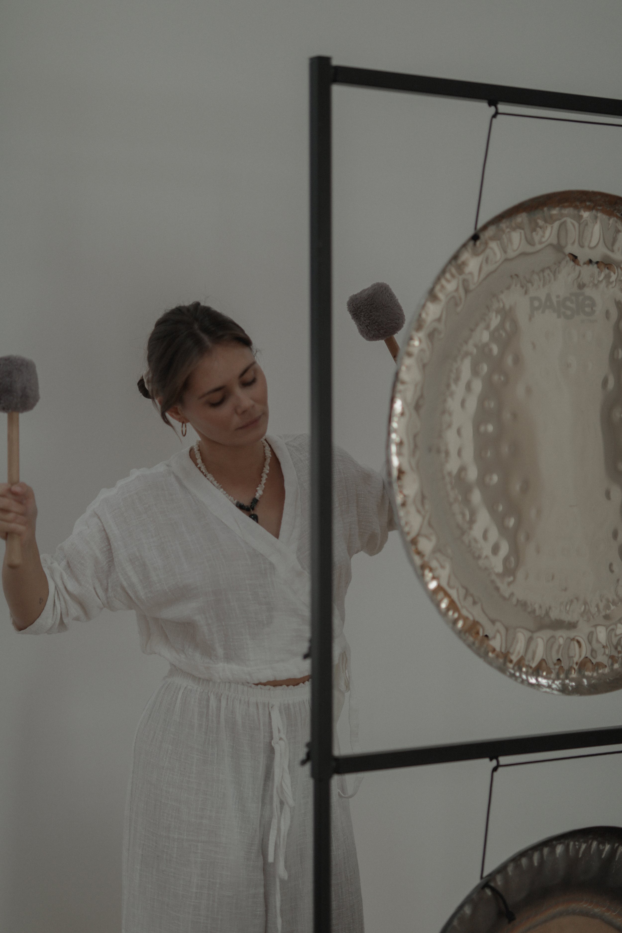 A woman dressed in white practicing sound healing with two mallets and large gongs.