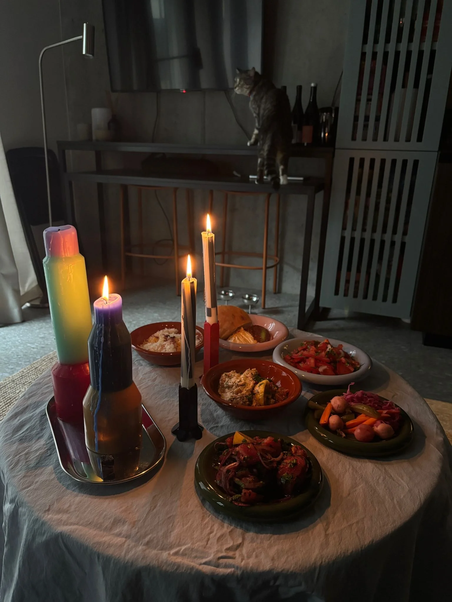 Table decorated for a celebration with candles and various dishes of food, with a cat sitting on a shelf in the background.