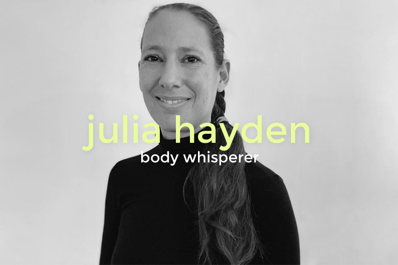 Black and white portrait of a woman with long hair in a braid, smiling slightly, wearing a dark top. Overlayed text reads 'julia hayden' in large yellow-green font and 'body whisperer' in smaller white font.