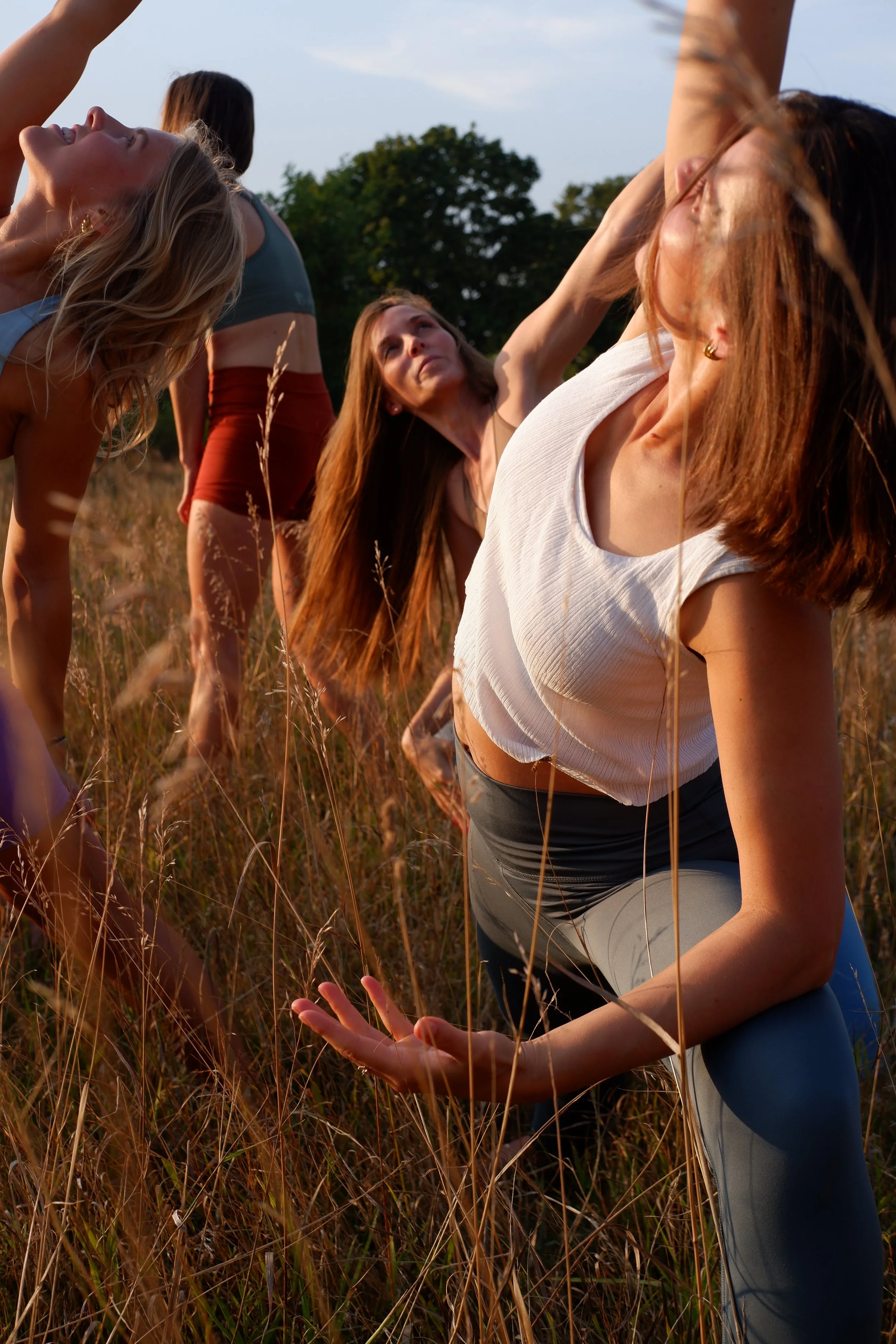 Four women practicing yoga outdoors in a grassy field during sunset.
