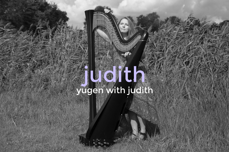 A woman standing outdoors in a field holding a harp, with overlay text "judith" and "yugen with judith."